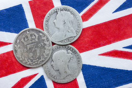 Three Queen Victoria silver threepences from the 19th century (from 1873, 1891, 1898) on a British flag. Concept representing history of the British Empire, Victorian time or old coin collecting.